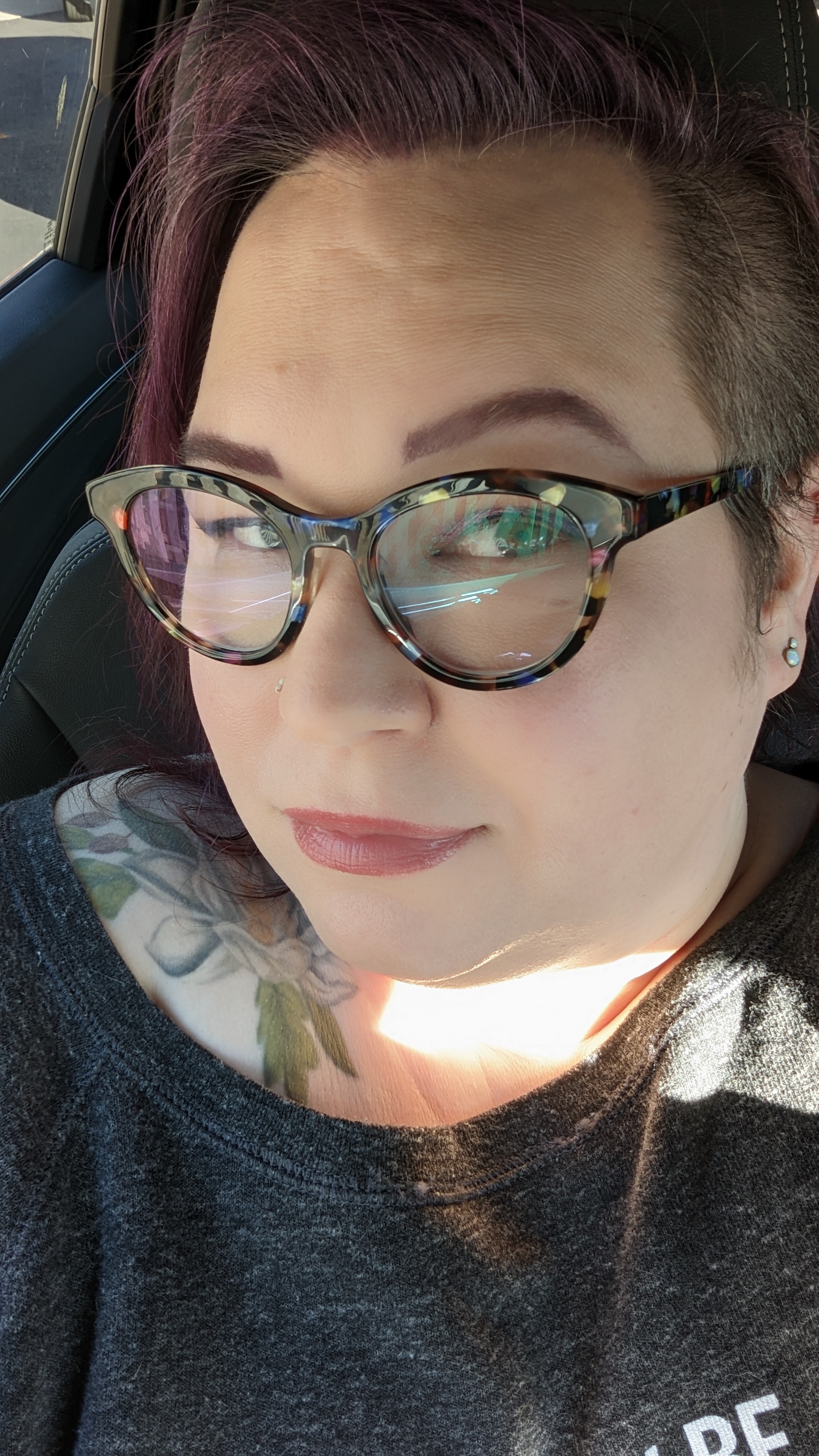 woman with purple hair, colorful glasses, and a tattoo of a magnolia on her shoulder