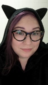 woman with purple hair and colorful glasses wearing a black hooded sweater with kitty ears