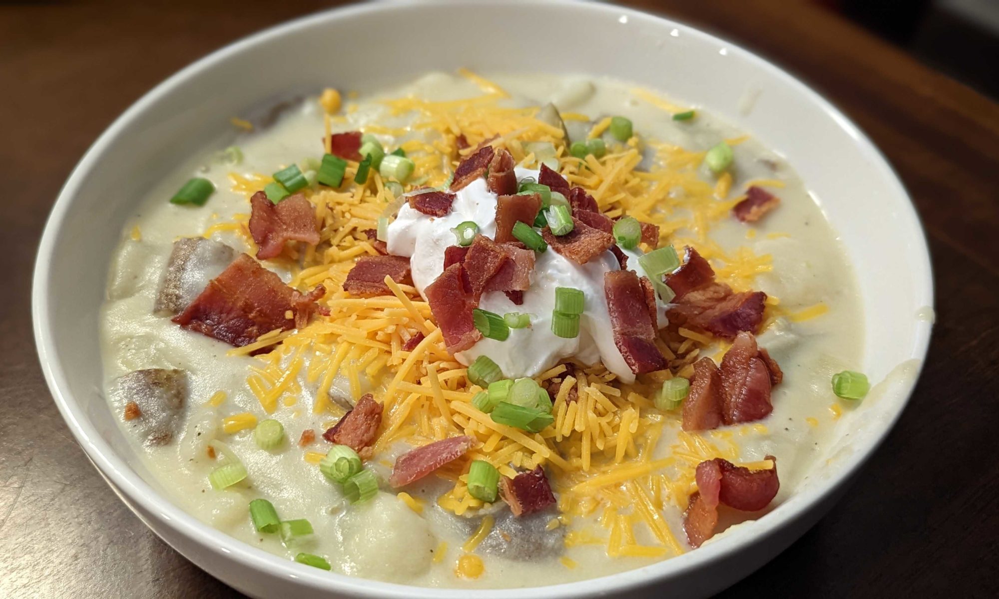 photo of a bowl of baked potato soup with scallions, cheese, bacon, and sour cream on top